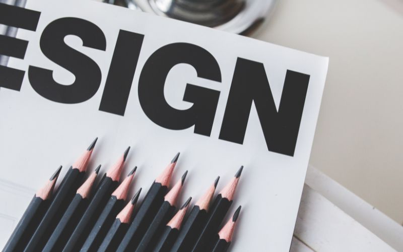 close up of bold typography word design printed on paper with neatly arranged black pencils representing creative logo design process