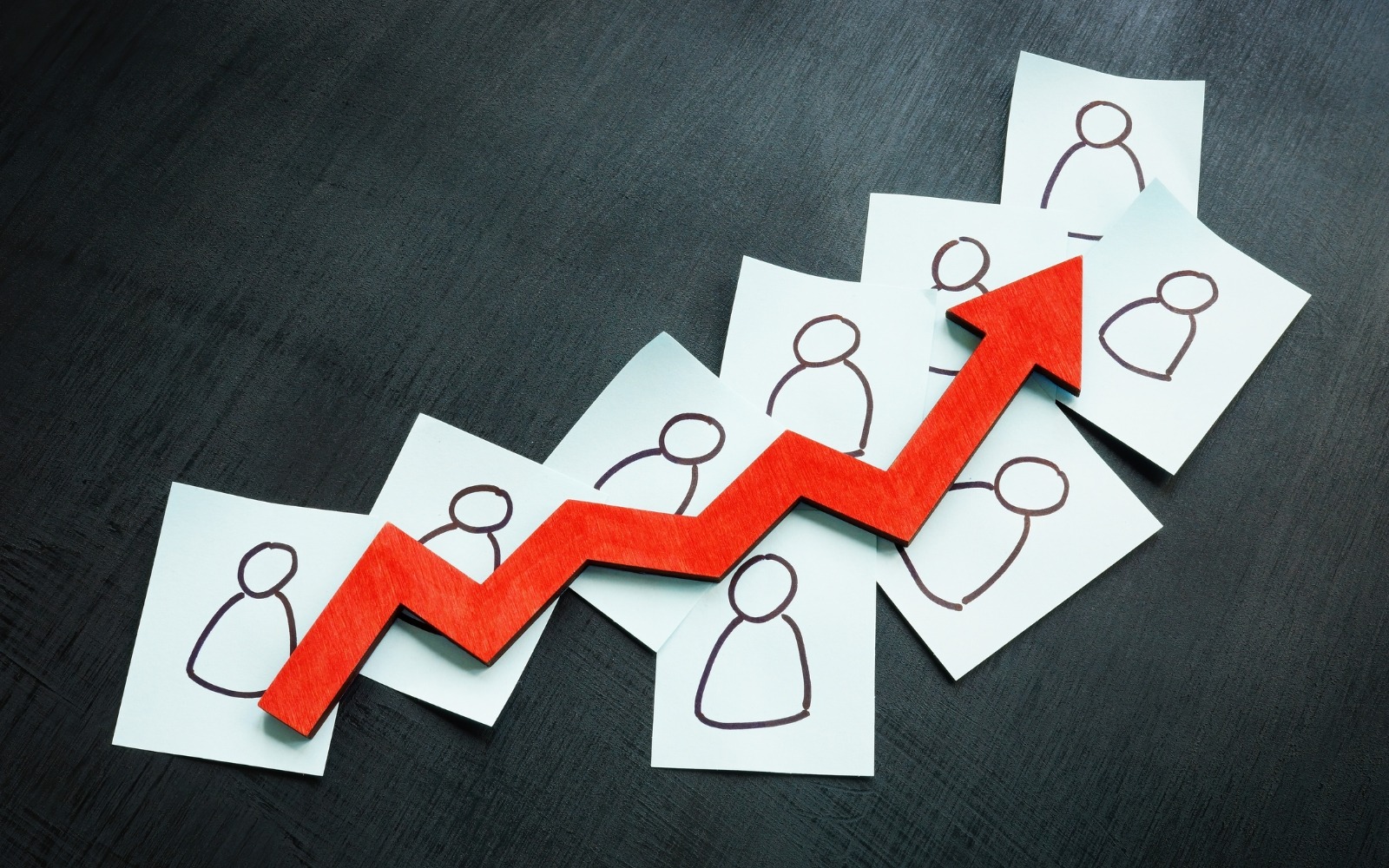 Rising red arrow over cards showing hand-drawn human figures representing growing B2B leads generated through organic search over a compounding timeline